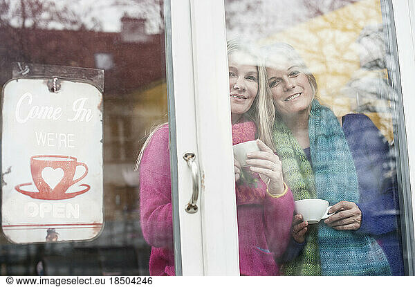 Two friends looking through window and drinking coffee in coffee shop  Bavaria  Germany