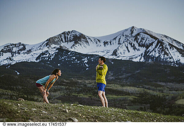 Two friends stretch together before trail running in the mountains