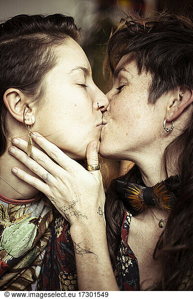 Two gay women kiss and smile in natural embrace at home