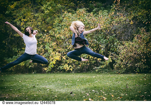 Two Girlfriends Leaping Through The Air Try Doing A Martial Arts Kick Move For Fun Outdoors In A Park On A Fall Evening  Edmonton  Alberta  Canada