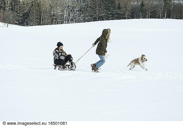 Two girls and a dog with slide in snowy landscape in winter  Bavaria  Germany