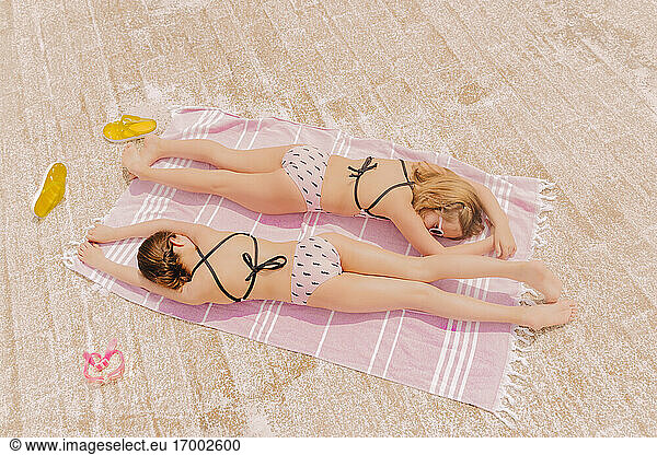 Two girls in swimsuits lying on blanket relaxing