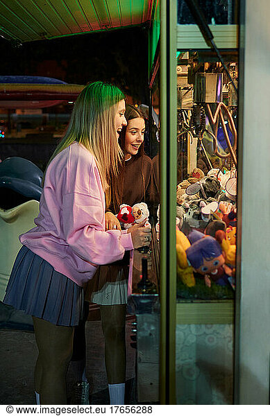 Two girls play in a claw machine to get soft toys