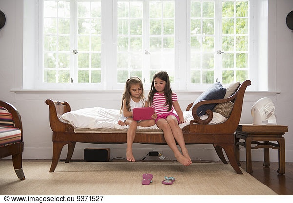 Two girls playing indoors  looking at a digital tablet.