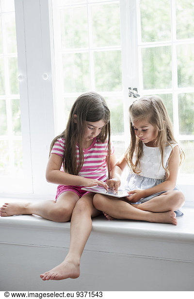 Two girls playing  sharing a digital tablet.