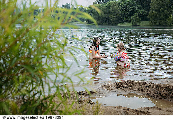 Two girls playing together on lake shore in sand