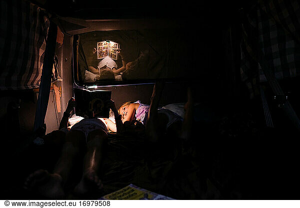 two girls reading at night by flashlight while camping in summertime