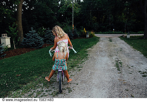 Two girls riding a bike down a driveway in the summer