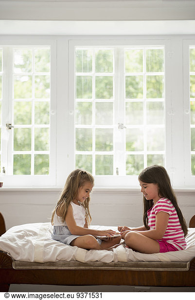 Two girls sitting and playing  using a digital tablet.