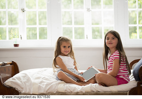 Two girls sitting holding a digital tablet.