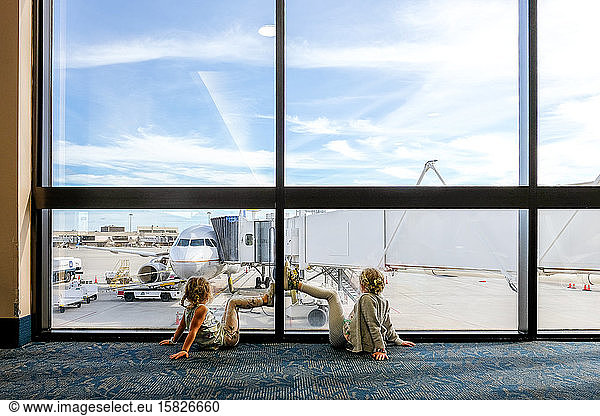 two girls sitting on floor in airport staring at airplane waiting