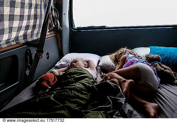 two girls sleeping in van while camping at dawn