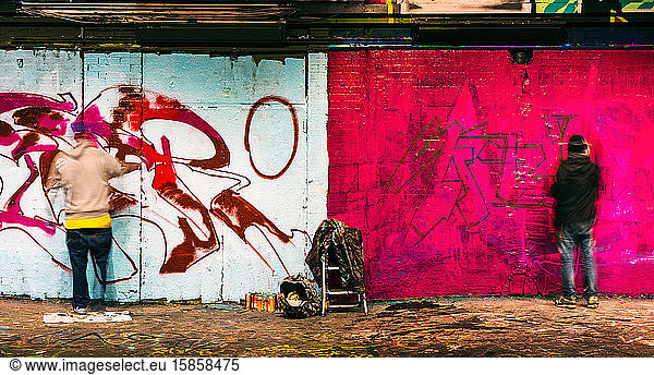Two graffiti artists painting a wall in Leake Street  London