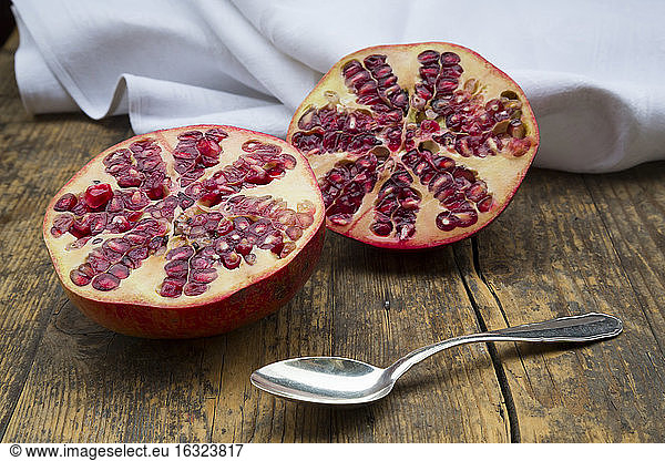 Two halves of a pomegranate and tea spoon on wood