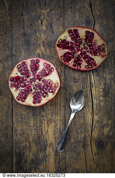 Two halves of a pomegranate and tea spoon on wood