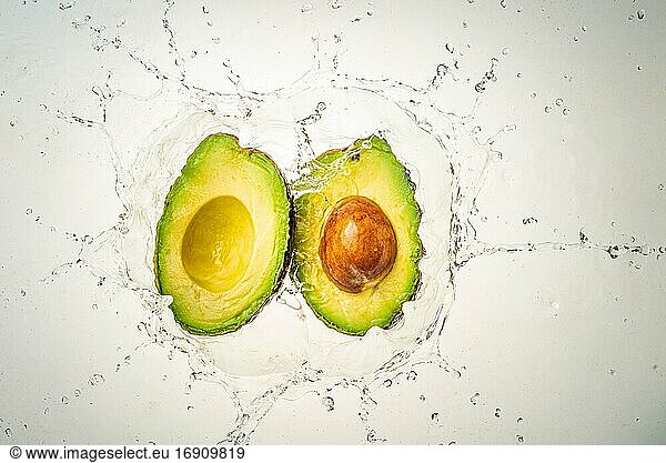 Two halves of avocado splashing into clear water  light background