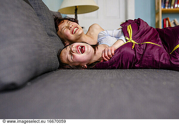 two happy children lay on couch together laughing out loud with joy