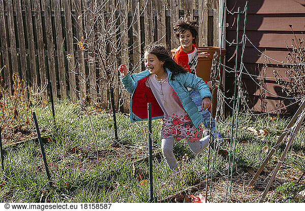 Two happy children play in sunshine in backyard garden