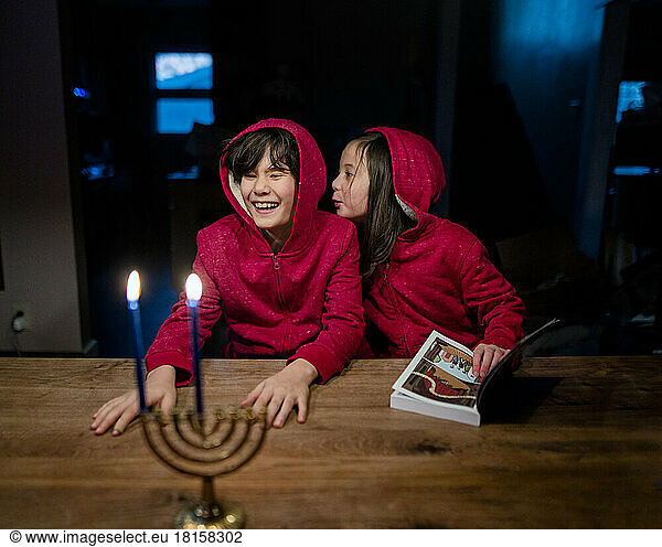 Two happy children sit at table with Hannukah candles