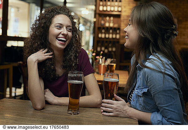 Two happy female friends having beer and socializing in a pub