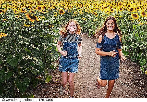 Two happy tween girls running in a sunflower field.