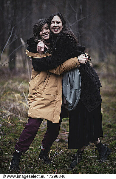 two happy women smile and embrace in winter coats in german forrest