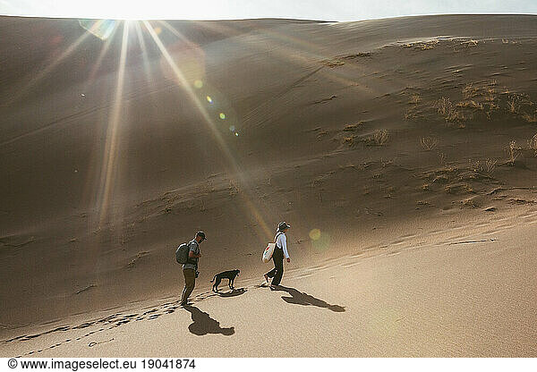 two hikers and their dog follow footprints in the sand dunes