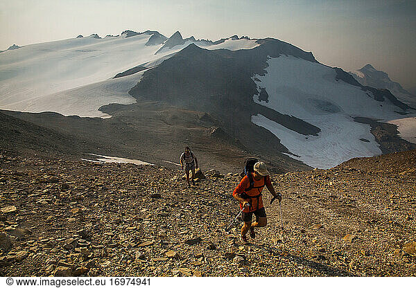 Two hikers climb towards the summit of Glacier Peak at dawn.