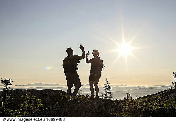 Two hikers high five and celebrate reaching summit of mountain  Maine