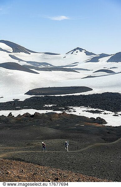 Two hikers on trail through lava sand  Barren hilly volcanic landscape of snow and lava fields  Fimmvörðuháls hiking trail  Þórsmörk Nature Reserve  Suðurland  Iceland  Europe
