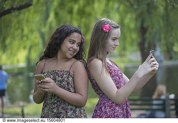 Two Hispanic teen sisters with braces looking at their cell phones in park