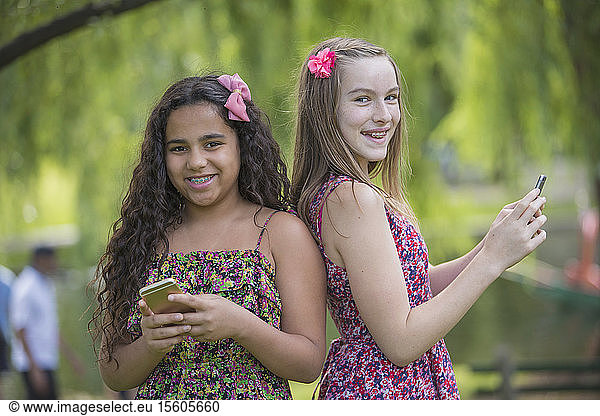 Two Hispanic teen sisters with braces using their cell phones in park