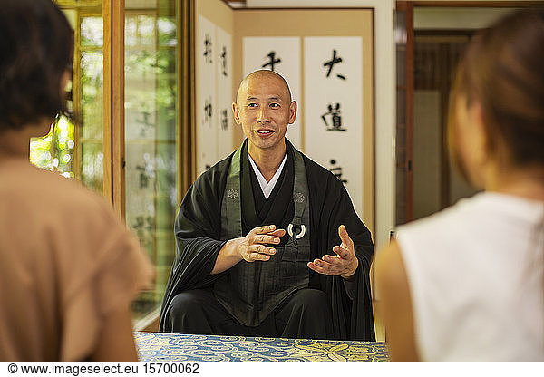 Two Japanese women and Buddhist priest kneeling in Buddhist temple  talking.