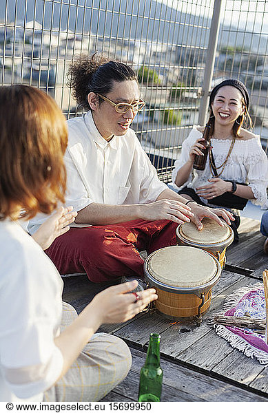 Two Japanese women and man sitting on a rooftop in an urban setting  playing drums.