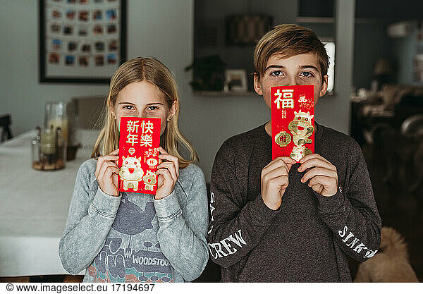 Two kids holding lunar new year envelopes in front of faces