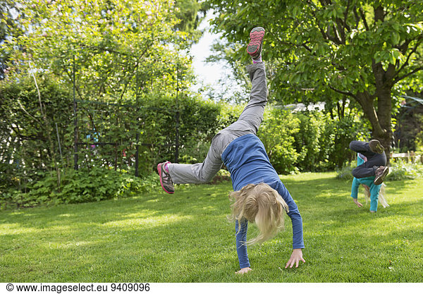 Two kids performing cartwheels on garden lawn