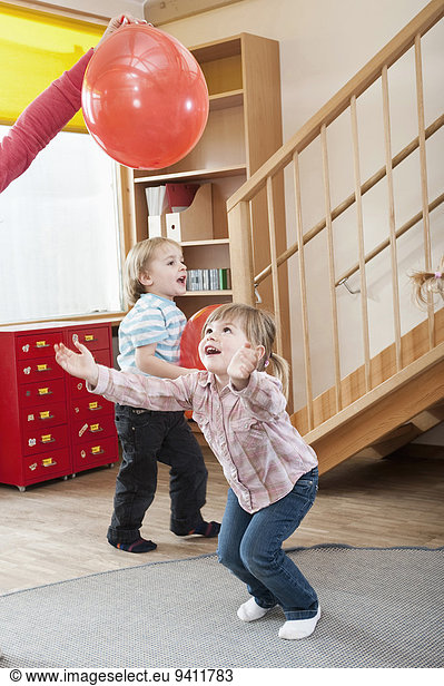 Two kids playing with red balloons in kindergarten