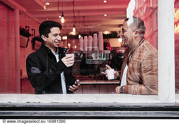 two latino young men talking while drinking coffee with a happy expression