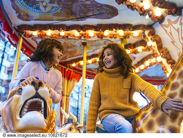 Two laughing little girls having fun on a carousel