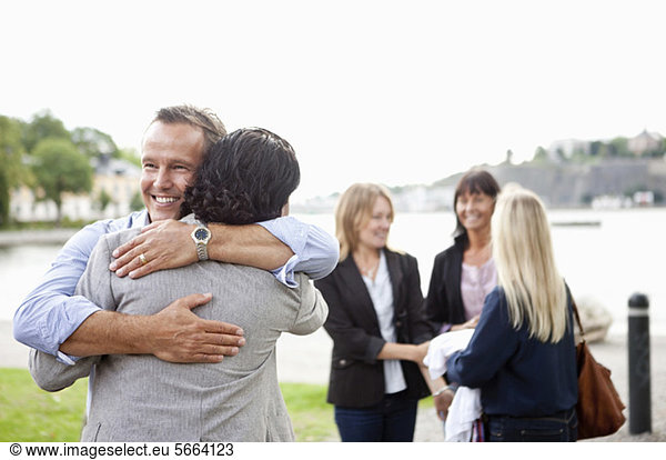 Two male friends hugging each other with female colleagues in background