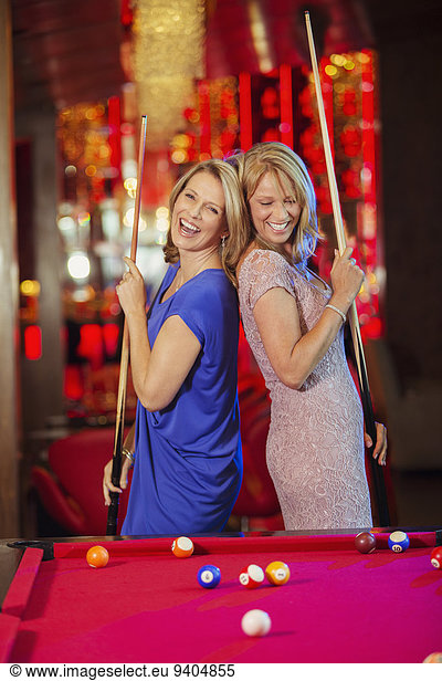 Two mature women laughing and playing pool in nightclub