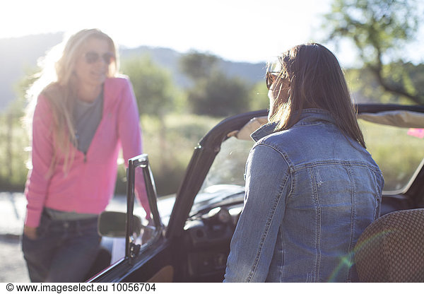 Two mature women  talking  beside convertible car