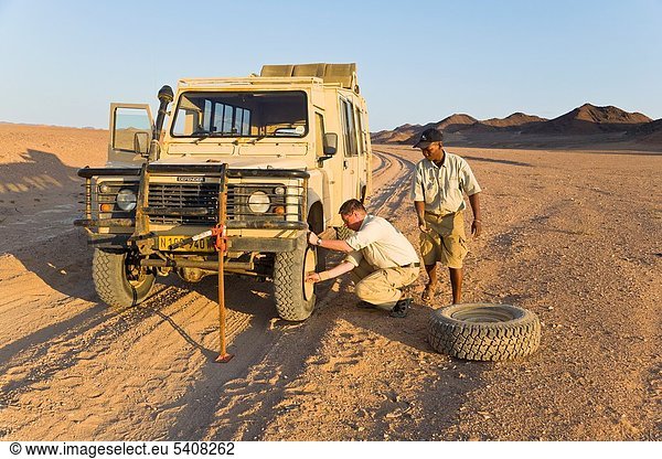 Two men changing a flat tyre in the desert  Namibia  Africa