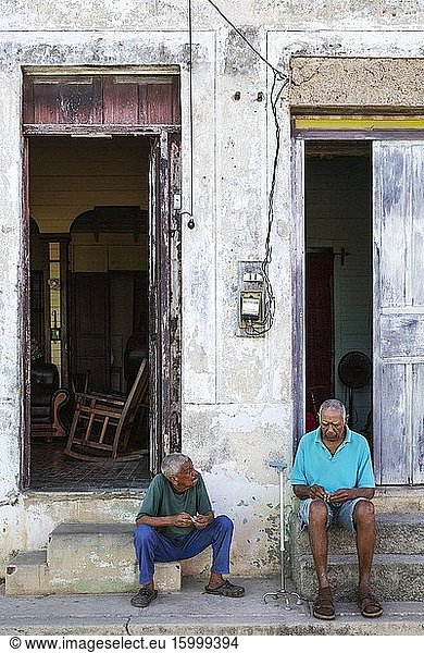 Two men having a chat at the doorsteps of their houses with decayed fa?ades of crumbling plaster and weathered wooden doors. Gibara  Cuba.