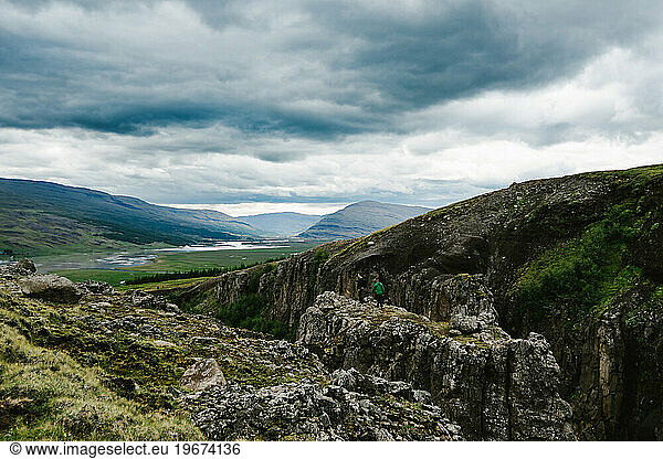 Two men hike on rock cliffs with clouds and valley beyond
