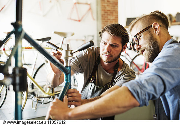 Two men in a cycle repair shop  looking at a bicycle.