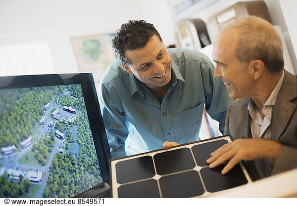Two men in an architecture office. Working on a green construction project  sitting by a screen. A man holding a tile sample.