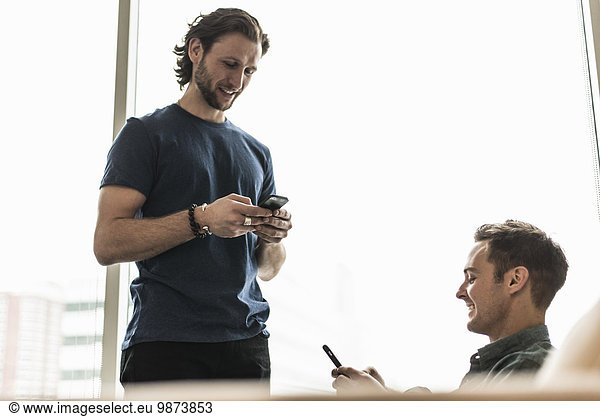 Two men in an office  checking their smart phones.