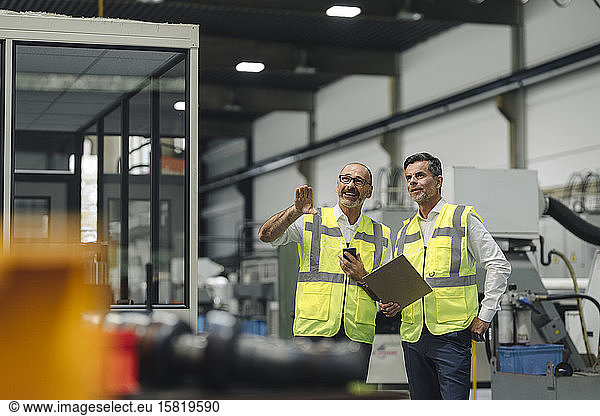 Two men in reflective vests talking in a factory