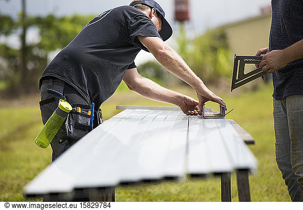 two men measure brackets for mounting solar panels.